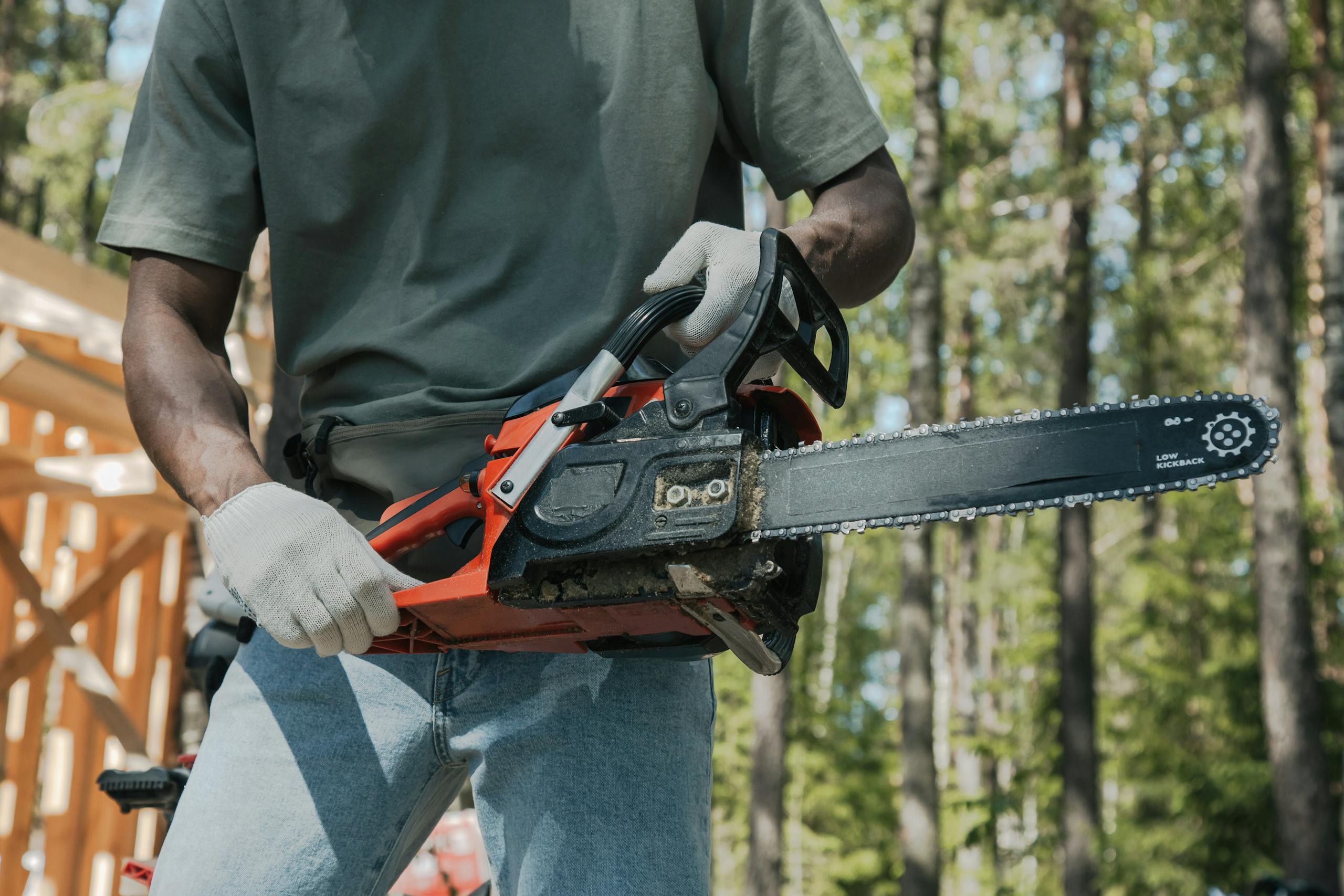 An adult holding a chainsaw outdoors, showcasing forest work equipment usage.